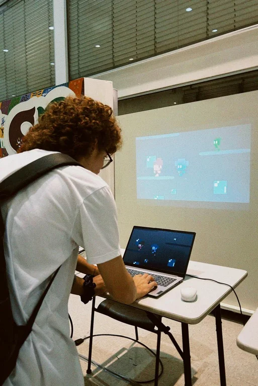 Visitante jogando no notebook com o jogo projetado ao fundo.