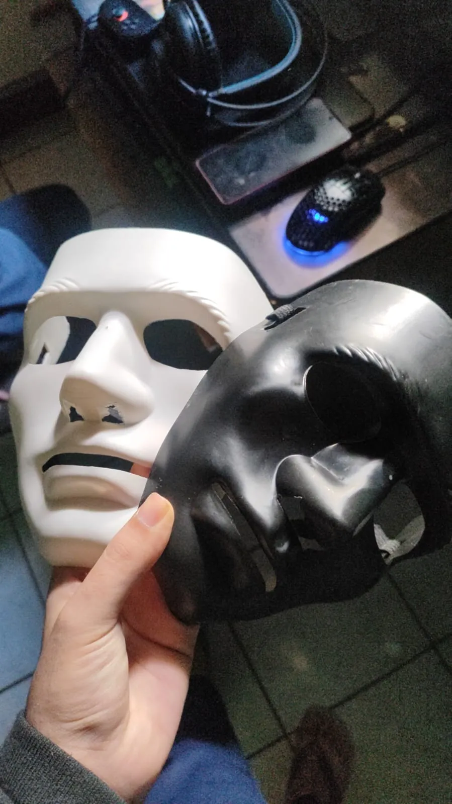 Mão segurando duas máscaras de teste, uma branca e uma preta.