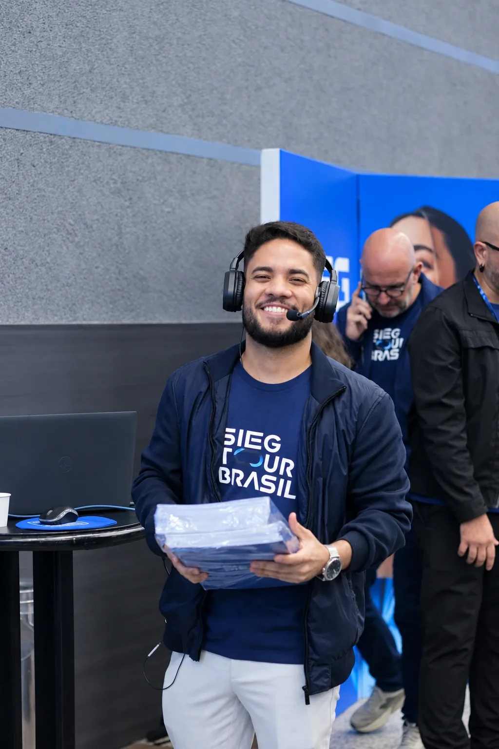 Membro da equipe SIEG com headset e camiseta do evento, sorrindo