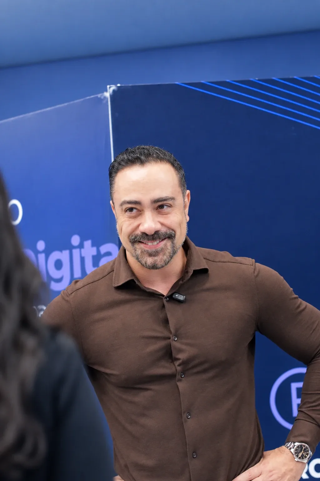Palestrante sorrindo em frente ao painel azul do evento