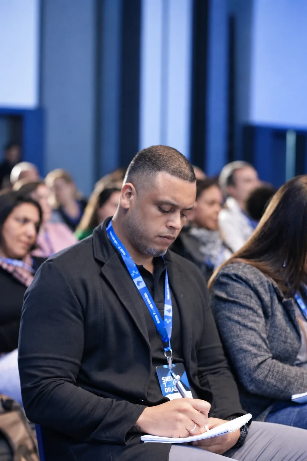 Participante anotando durante a palestra, com a plateia ao fundo